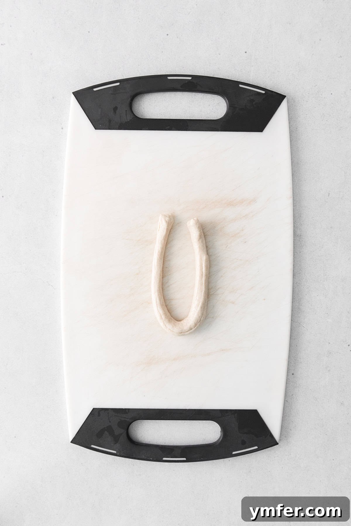 A piece of pretzel dough skillfully shaped into a U-bend on a cutting board, ready for the next step.