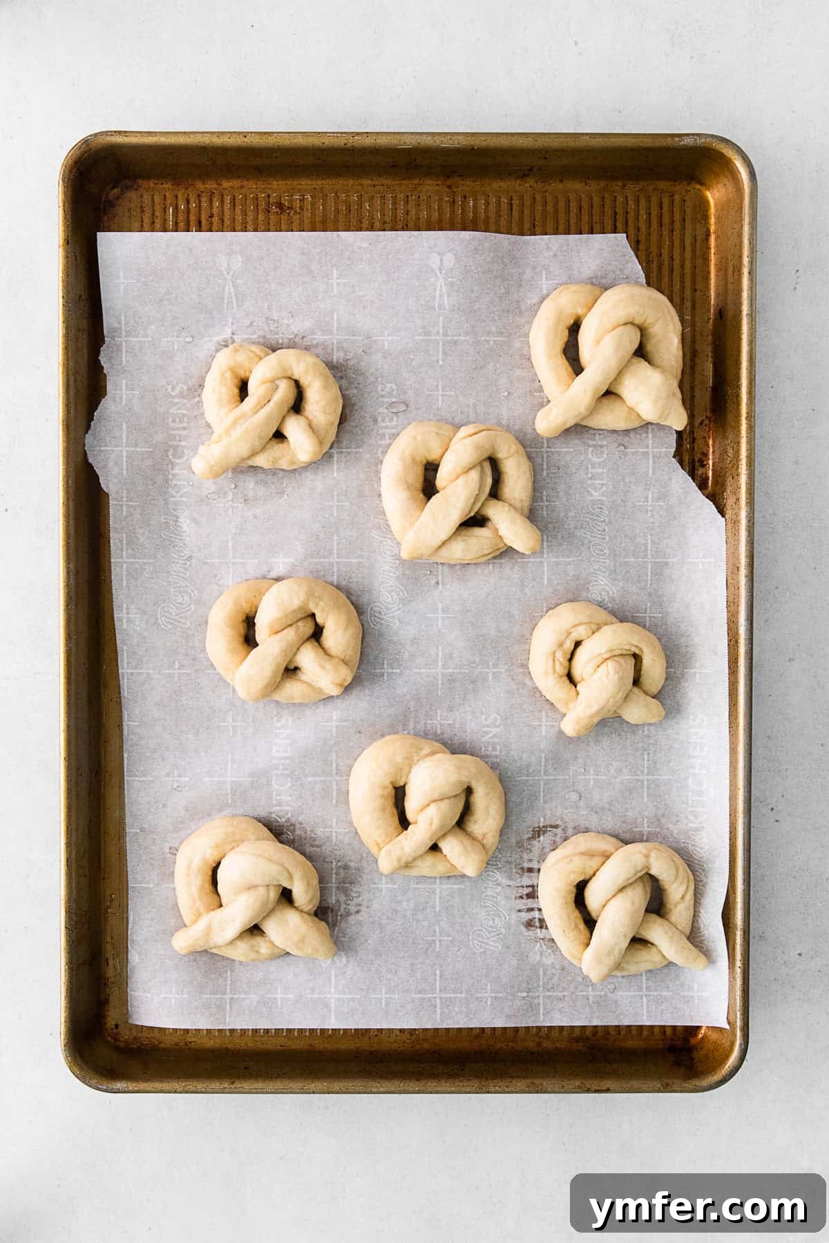 Several uncooked, shaped soft pretzels neatly arranged on a baking tray, ready for the boiling process.