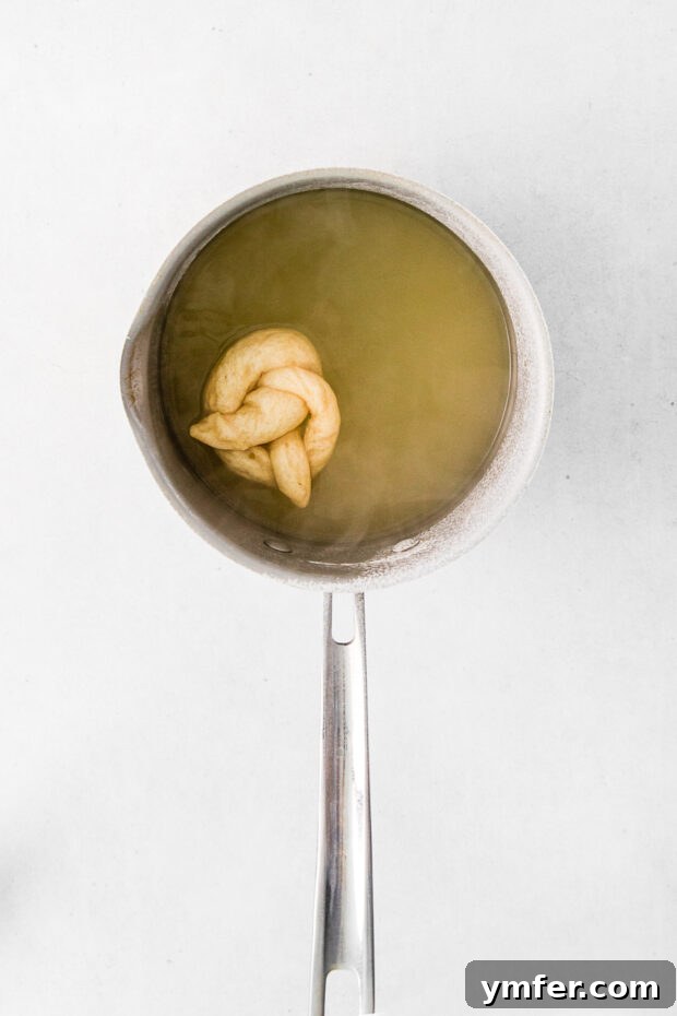 A shaped pretzel being carefully lowered into a pot of boiling baking soda water, crucial for its unique texture.