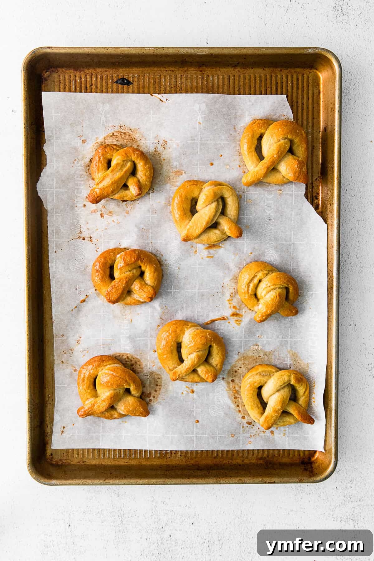 A batch of golden-brown, cooked soft pretzels resting on a baking tray after being removed from the oven.