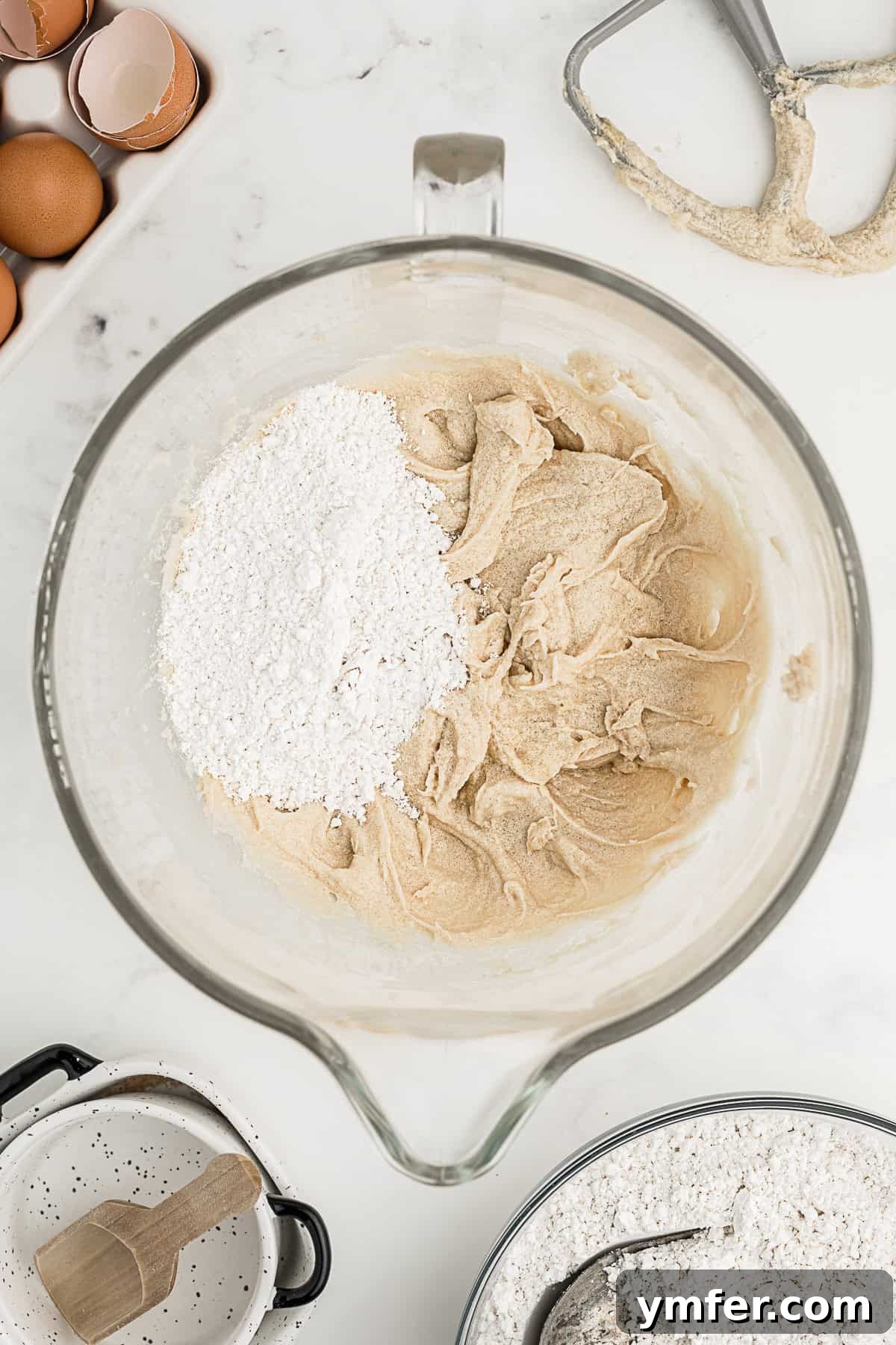 Ultimate Chocolate Chip Cookie Cake 5 Cookie batter in a mixing bowl with dry ingredients, specifically flour, being added to the wet mixture, showing the next step in dough preparation.