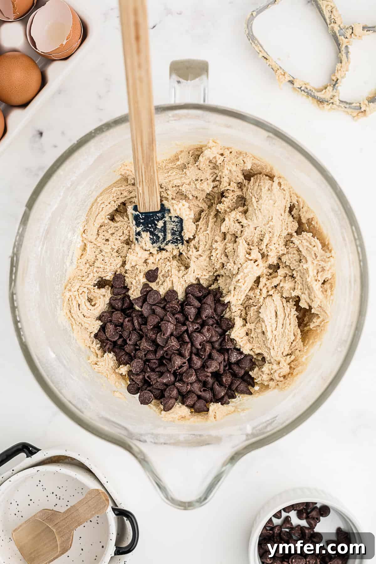 Ultimate Chocolate Chip Cookie Cake 6 A spatula gently folding chocolate chips into a bowl of prepared cookie batter, illustrating the final stage of dough mixing.