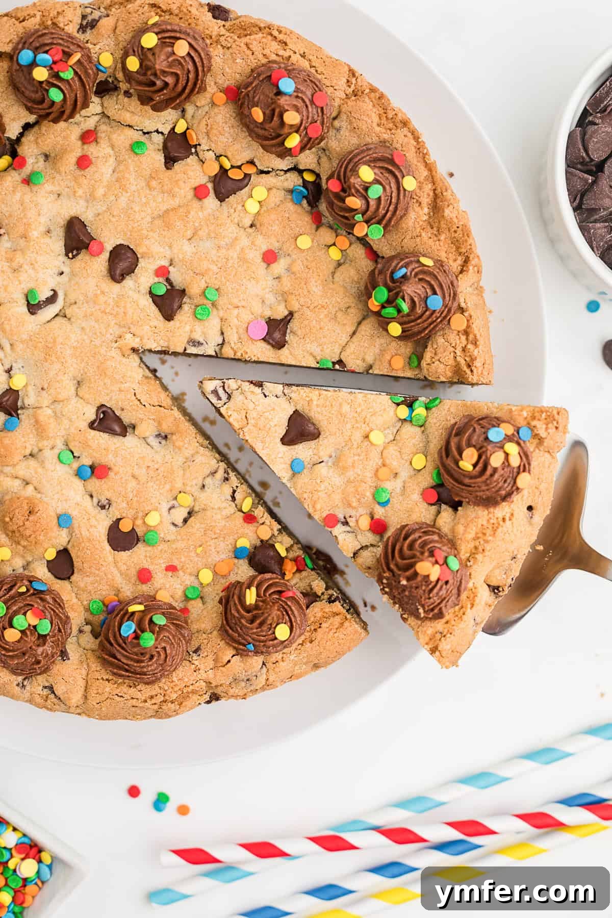 Ultimate Chocolate Chip Cookie Cake 7 A hand gently removing a perfectly sliced piece of Chocolate Chip Cookie Cake from the round cake, revealing its soft interior.