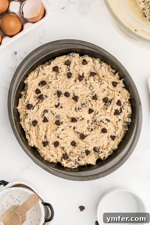 Ultimate Chocolate Chip Cookie Cake 9 An uncooked Chocolate Chip Cookie Cake batter spread evenly in a round baking pan, ready to be placed in the oven.