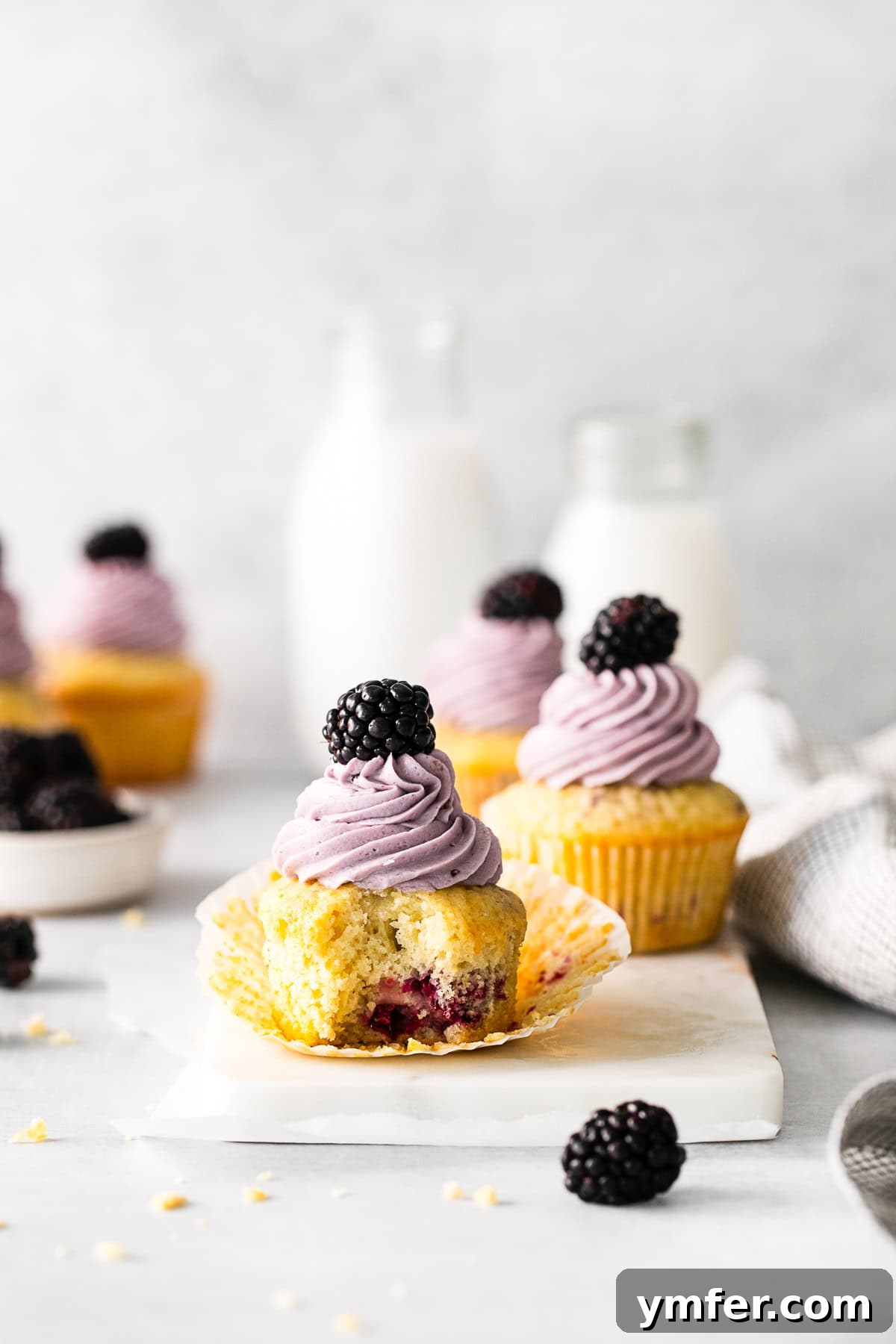 Blackberry Bramble Cupcakes 2 A Blackberry Cupcake with a bite taken out of it, revealing the fluffy interior and berry pieces.