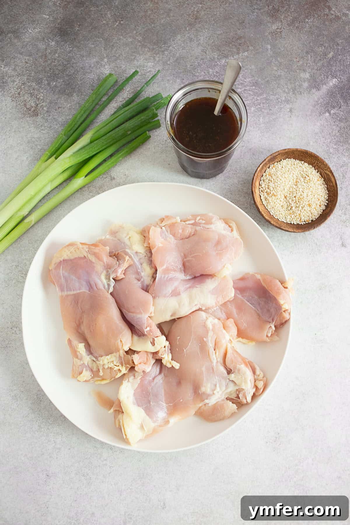 Raw chicken thighs ready for marinating next to a bowl of homemade teriyaki sauce.