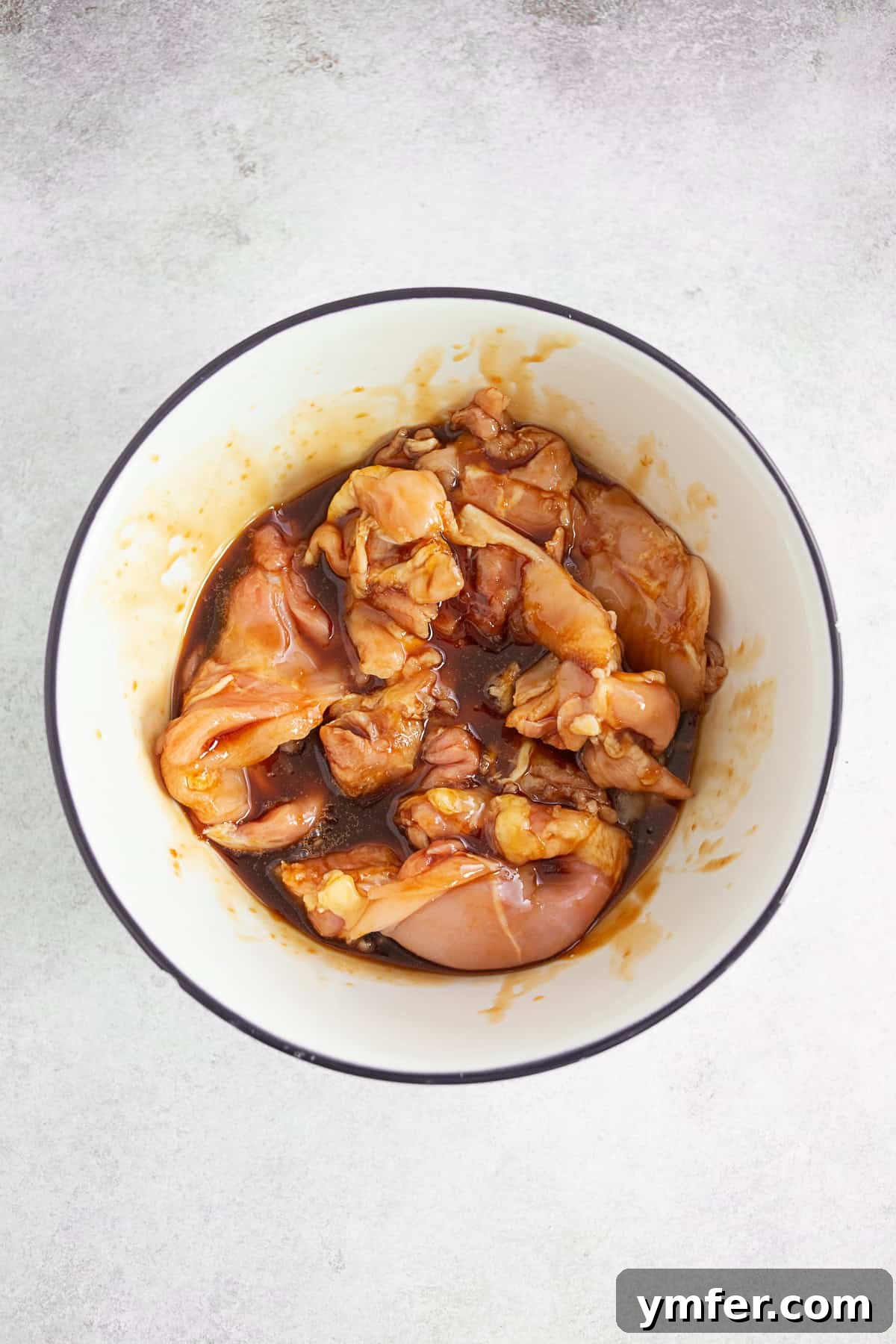 Boneless chicken thighs marinating in a glass bowl with teriyaki sauce.