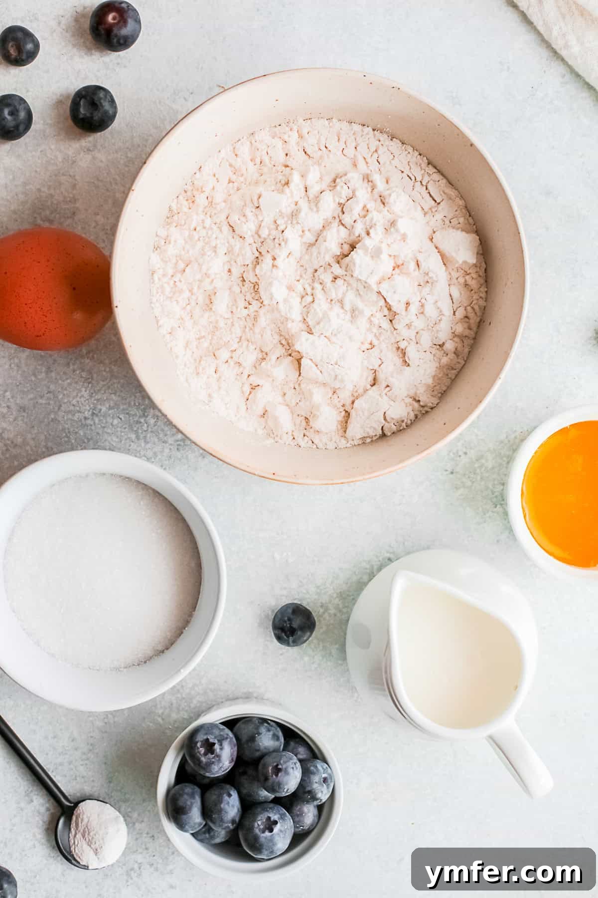 A collection of fresh ingredients laid out for making Baked Blueberry Streusel Donuts, including flour, sugar, eggs, butter, buttermilk, and fresh blueberries.