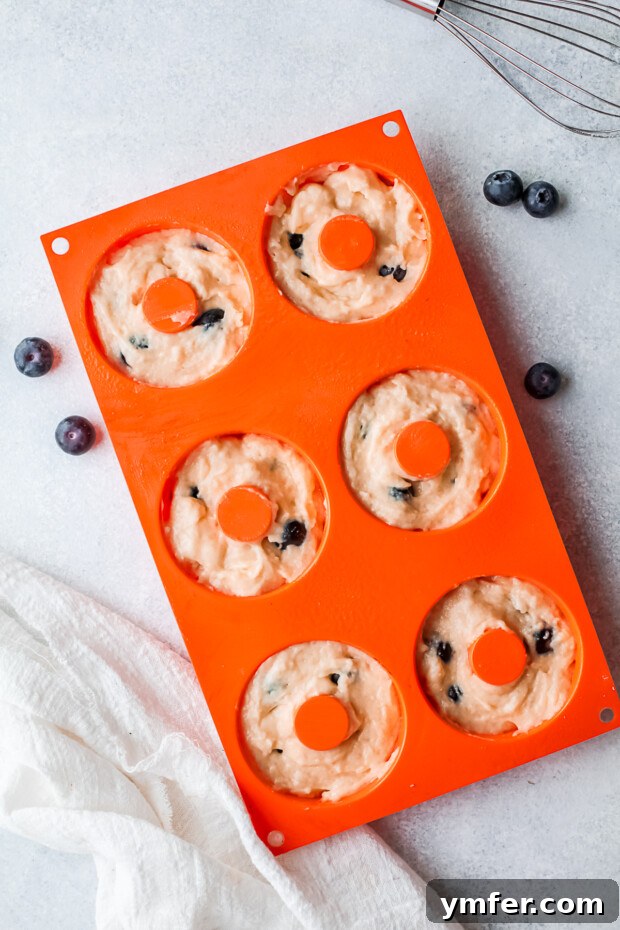 Uncooked blueberry donut batter in a non-stick donut pan, topped with streusel.