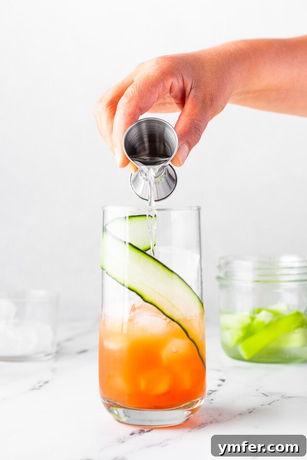 Grapefruit Gin Sparkler 5 Pouring aromatic gin into a cocktail glass, adding the spirit base to the Grapefruit Gin Fizz.