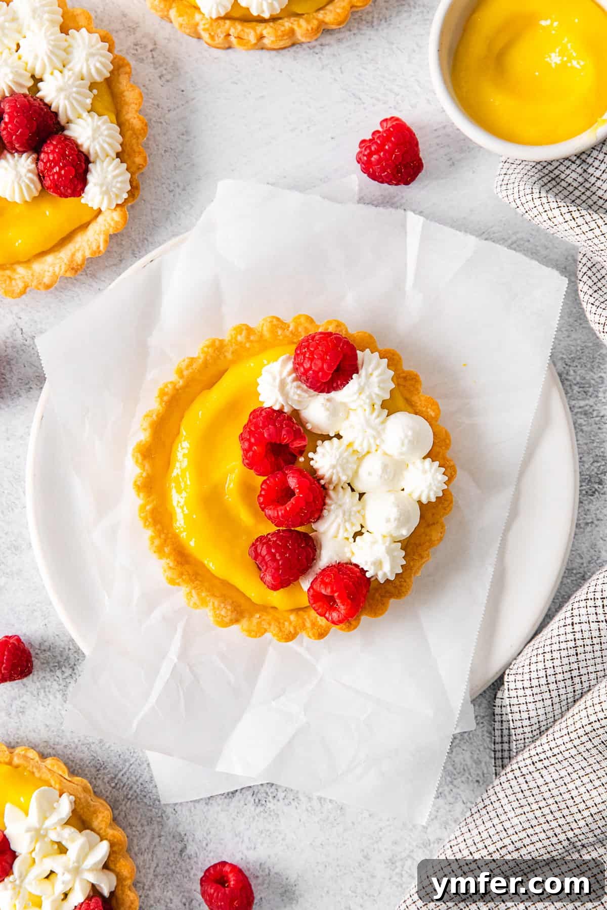 Sunshine Lemon Tarts 2 A plate of beautifully golden lemon curd tarts, garnished with fresh raspberries and whipped cream.