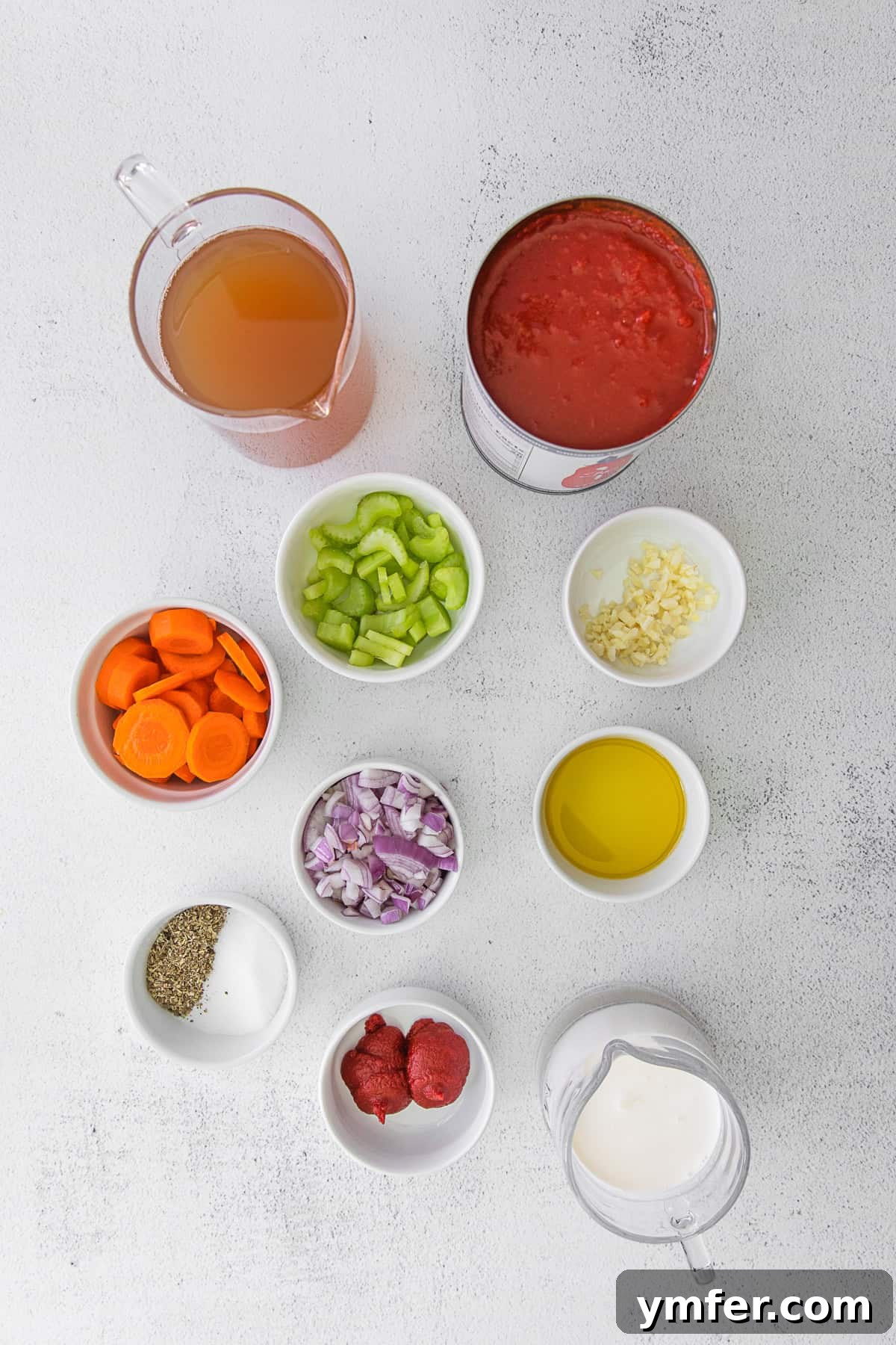 Effortless Instant Pot Tomato Delight 3 Ingredients to make Instant Pot Tomato Soup. A flat lay photo showing various fresh ingredients laid out, including olive oil, whole carrots, shallots, celery stalks, garlic cloves, a can of crushed tomatoes, a tube of tomato paste, a bowl of granulated sugar, and a small dish of Italian seasoning.