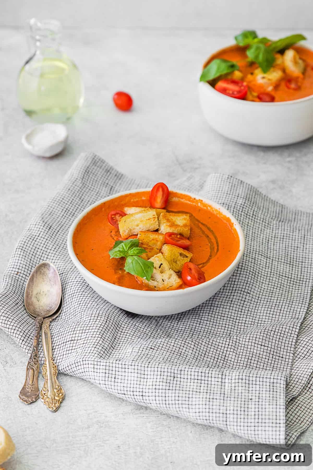 Effortless Instant Pot Tomato Delight 7 Instant Pot Tomato Soup served with a spoon and fresh basil. A white bowl of creamy Instant Pot Tomato Soup, garnished with fresh basil leaves and a spoon resting in it.