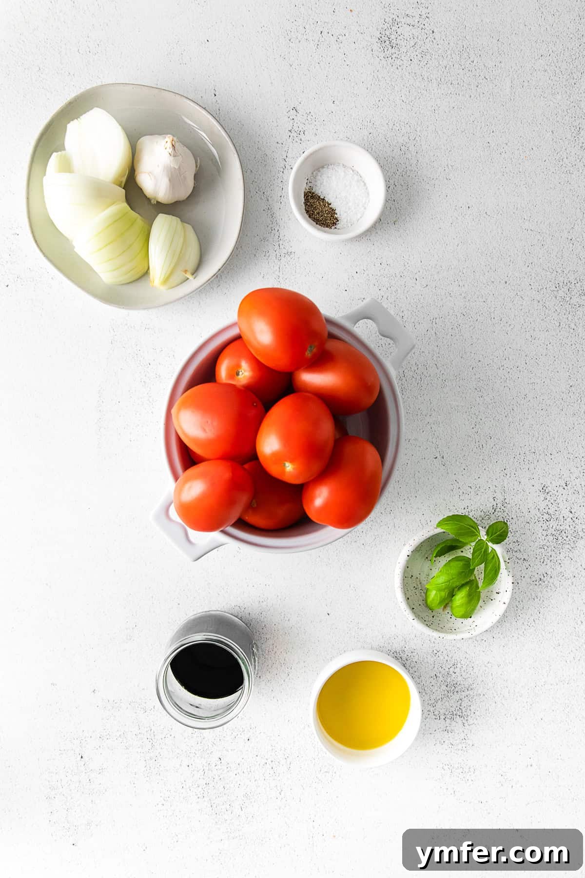 Richly Roasted Tomato Sauce 3 An assortment of fresh ingredients laid out on a table: Roma tomatoes, a sweet onion, whole garlic head, fresh basil leaves, a bottle of olive oil, balsamic vinegar, and a sprinkle of kosher salt.