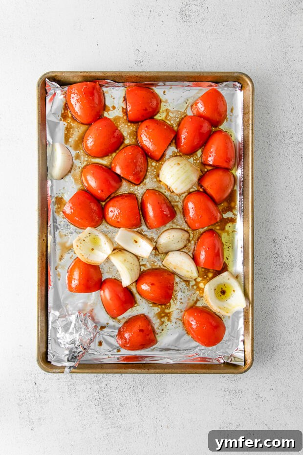 Richly Roasted Tomato Sauce 4 Whole Roma tomatoes and quartered sweet onions spread evenly on a foil-lined baking sheet, ready for roasting.