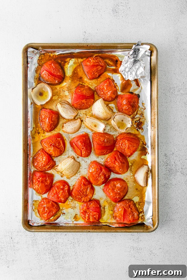 Richly Roasted Tomato Sauce 5 Roasted Roma tomatoes and caramelized onions on a baking sheet, showing their softened texture and slightly browned edges after cooking.