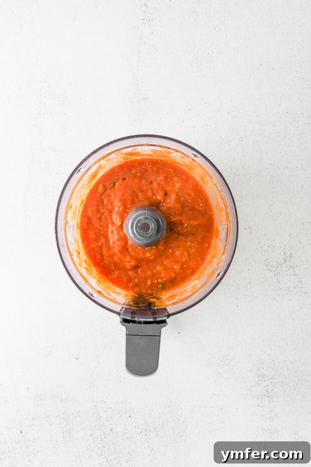 Richly Roasted Tomato Sauce 7 Smooth, pureed roasted tomato sauce in a food processor, showcasing its rich texture and color after blending.