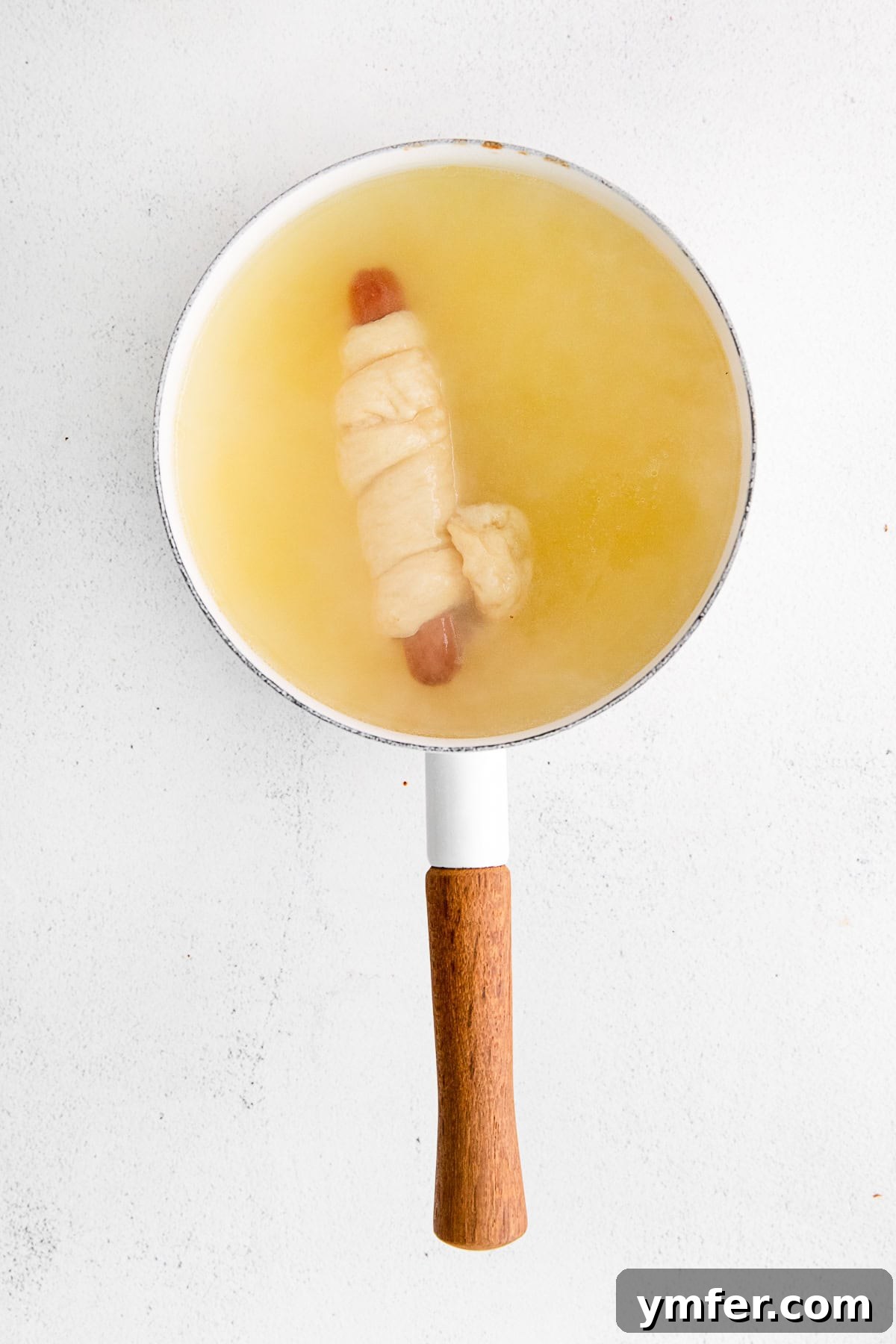 Golden Pretzel Franks 5 A partially cooked Soft Pretzel Dog floating in a pot of water during the baking soda bath, crucial for its pretzel texture.