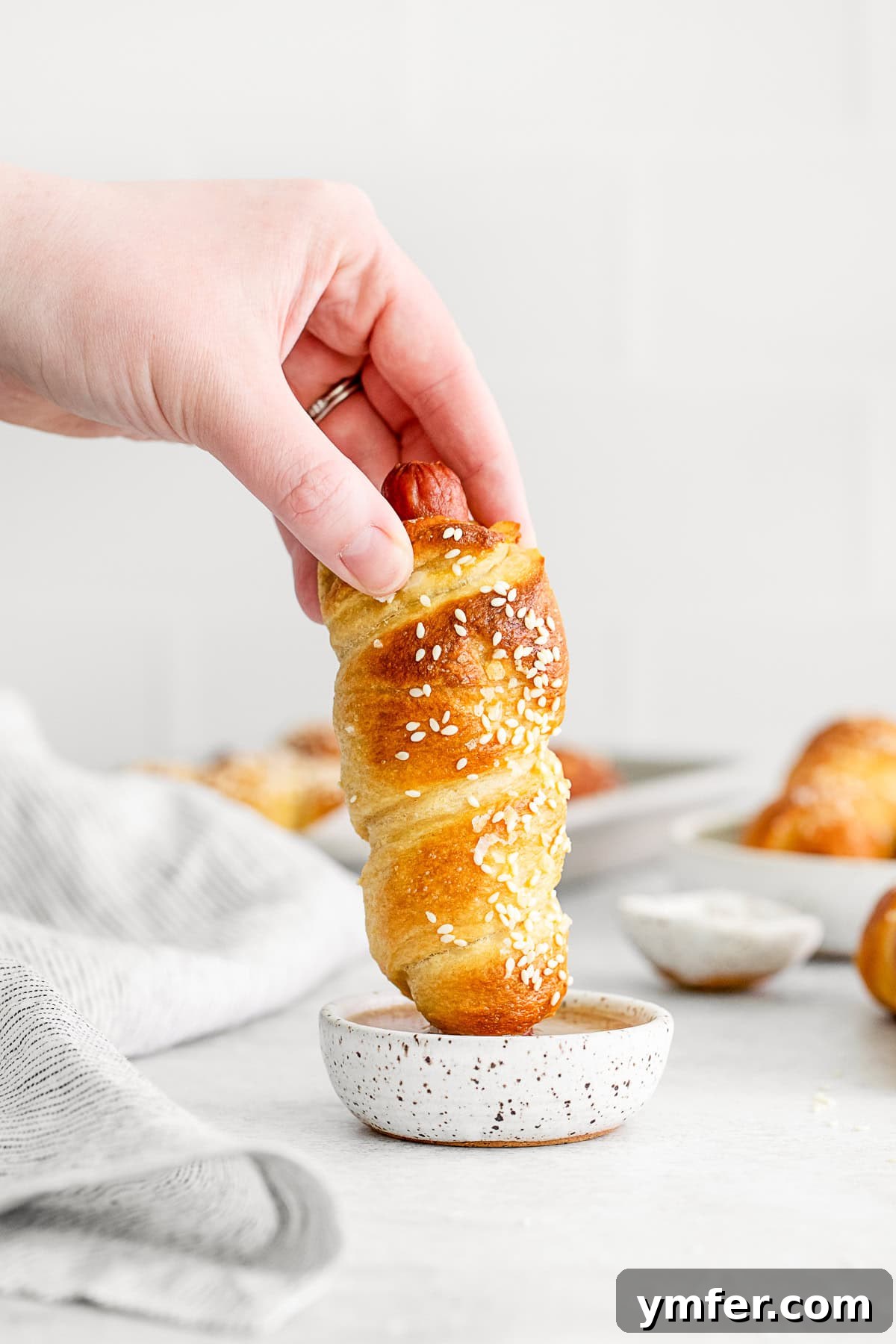 Golden Pretzel Franks 6 A Soft Pretzel Dog being dipped into a bowl of golden honey mustard sauce, showcasing a delicious pairing.