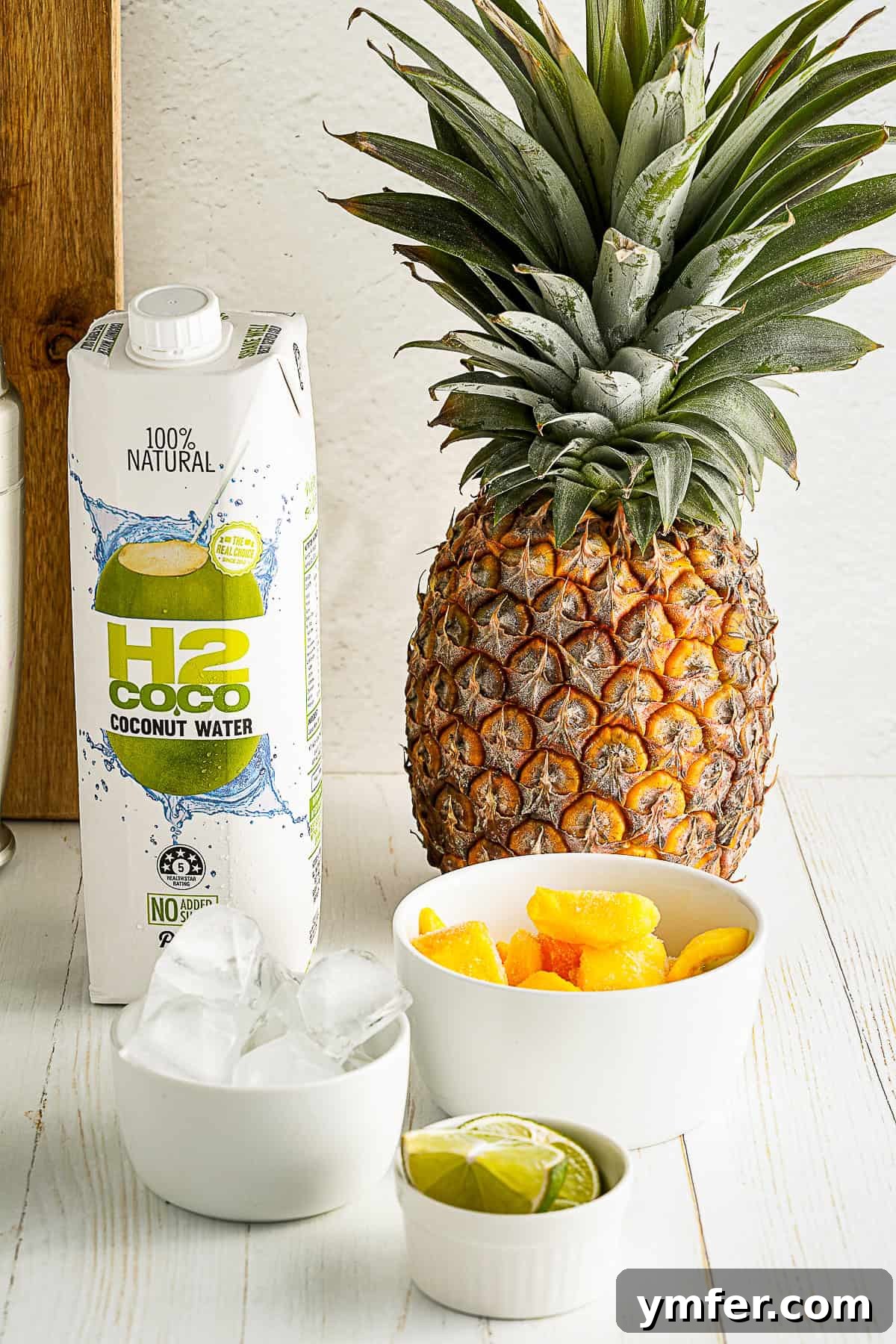 Tropical Mango Pineapple Bliss 3 Fresh ingredients for Mango Pineapple Smoothie laid out on a table, including frozen fruits, coconut water, and limes.