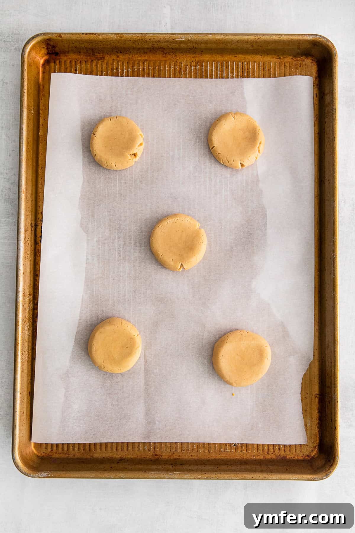 Maple Drizzle Delights 5 Uncooked maple cookie dough balls, flattened into discs, on a baking sheet pan.