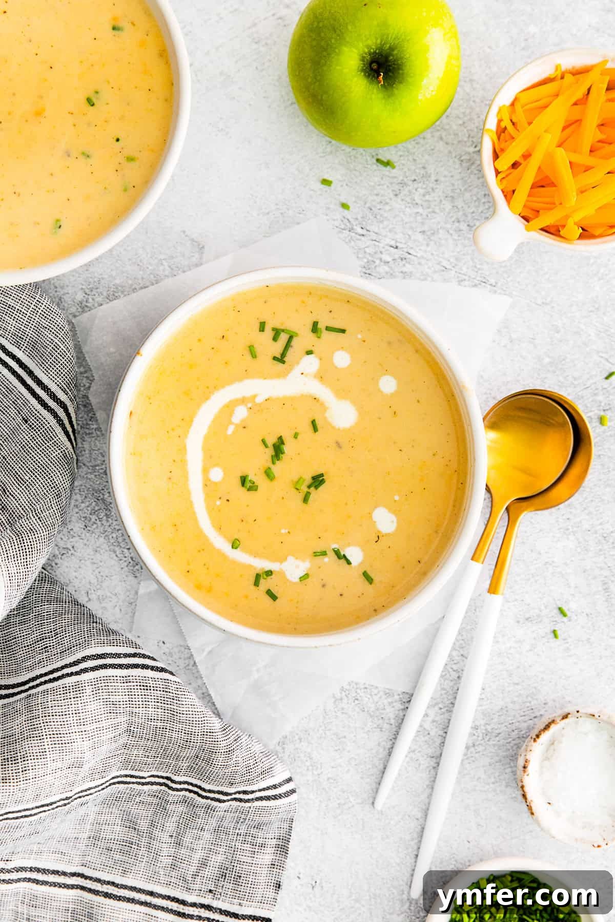 Creamy Cheddar Apple Harmony 2 Apple Cheddar Soup in a white bowl with a drizzle of sour cream on top.