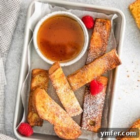 Crispy Air Fryer French Toast Sticks served with maple syrup on a white plate, highlighting their appetizing golden hue.