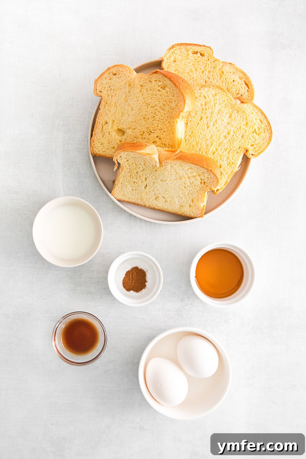 A vibrant display of fresh ingredients for Air Fryer French Toast Sticks, including brioche bread, eggs, milk, maple syrup, vanilla, and cinnamon, arranged on a kitchen table.