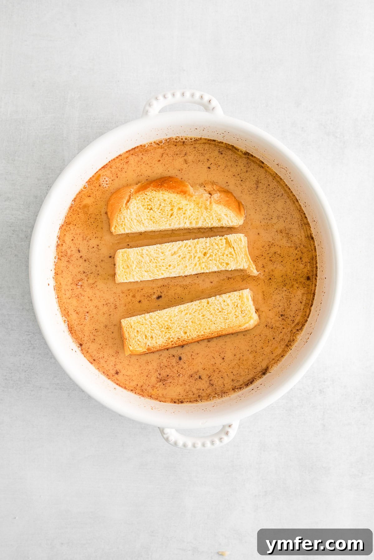 Thick slices of brioche bread, cut into sticks, soaking in a bowl of sweet maple custard, preparing for their air fryer transformation.