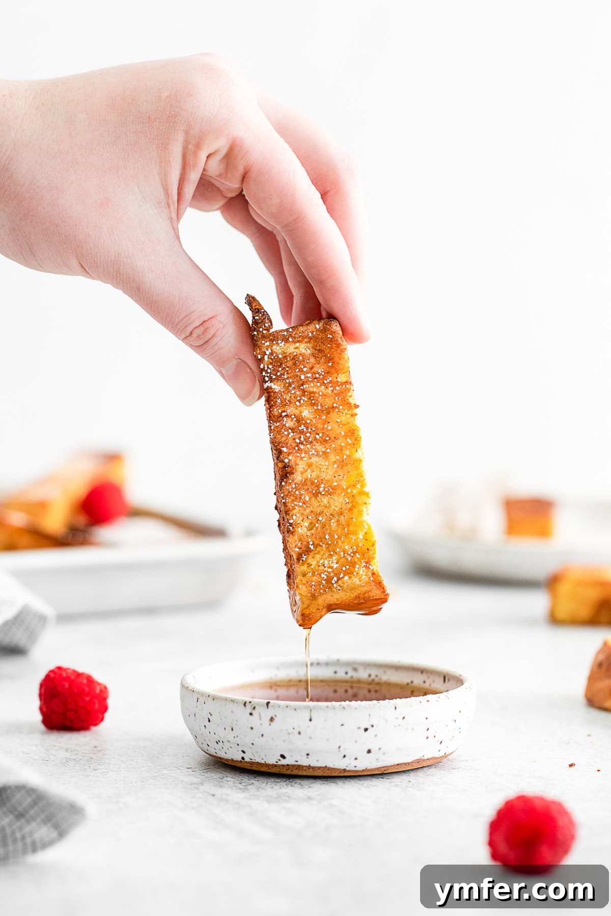 A crispy Air Fryer French Toast Stick being dipped into a small bowl of golden maple syrup, highlighting its perfect texture.