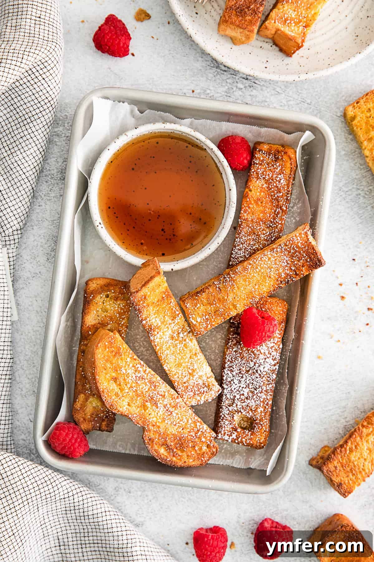 A close-up shot of golden Air Fryer French Toast Sticks, beautifully arranged on a white plate with a side of pure maple syrup, showcasing their inviting texture.