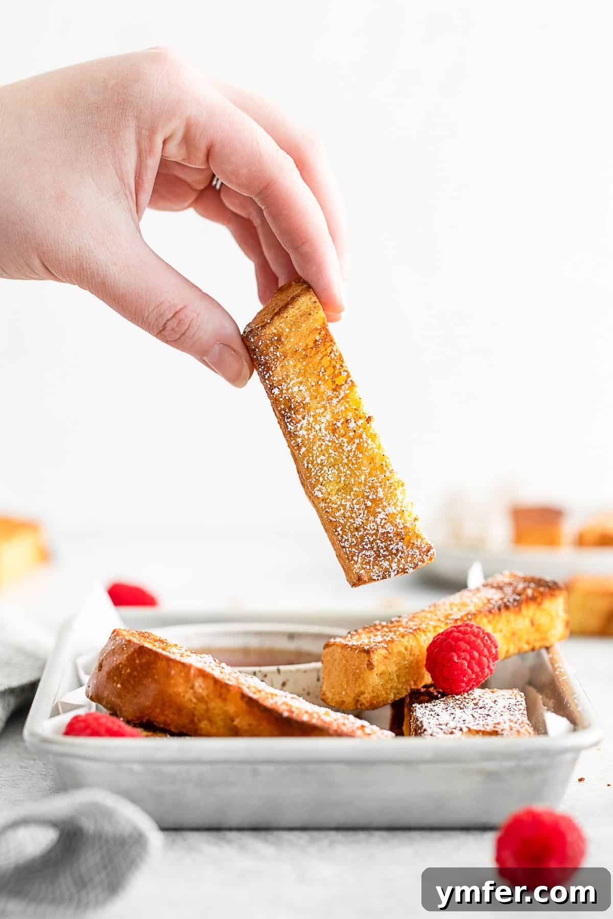 A hand picking up a french toast stick. 