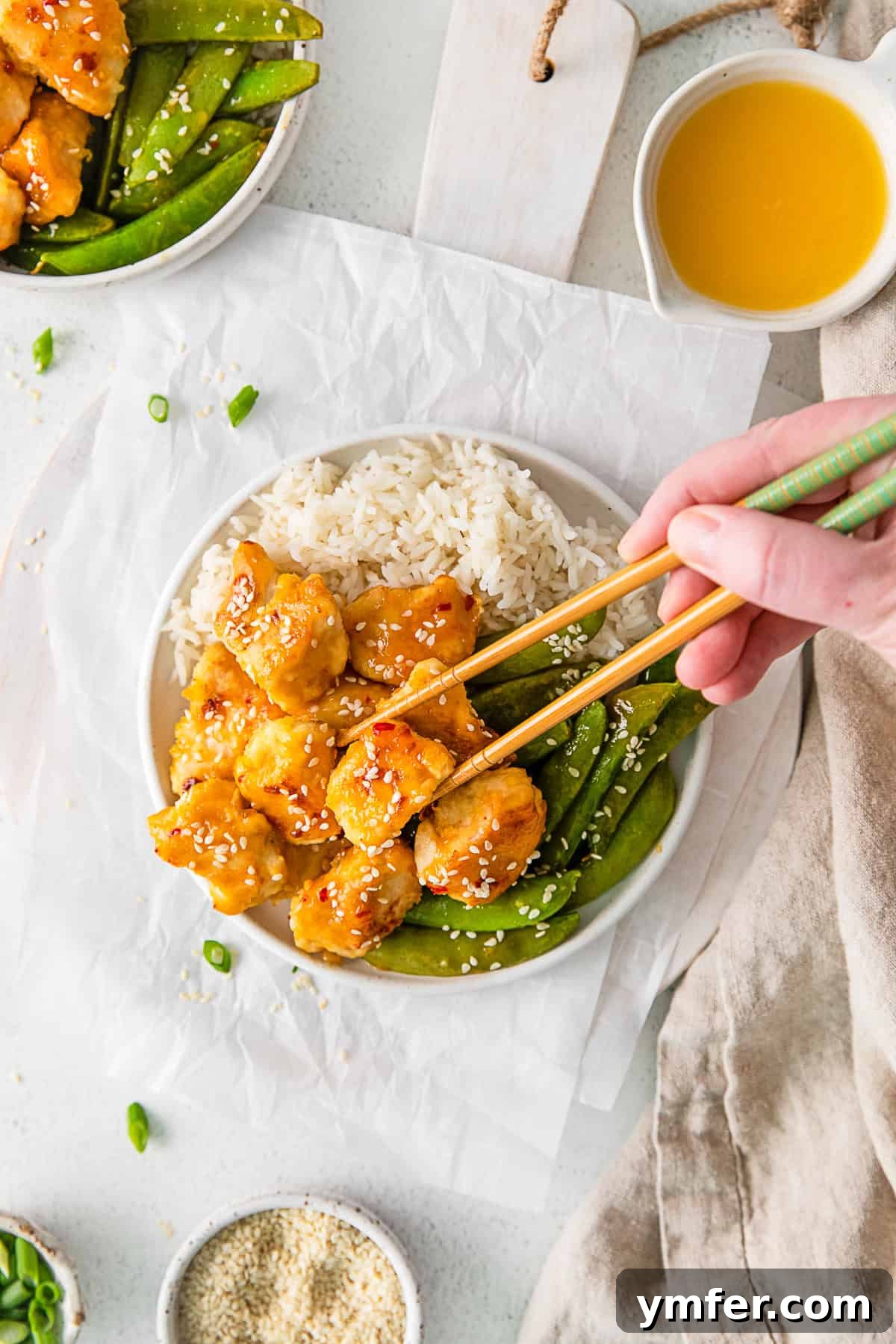 Simple Sheet Pan Sticky Orange Chicken 2 Sheet Pan Orange Chicken on a plate with chopsticks, garnished with sesame seeds and green onions.