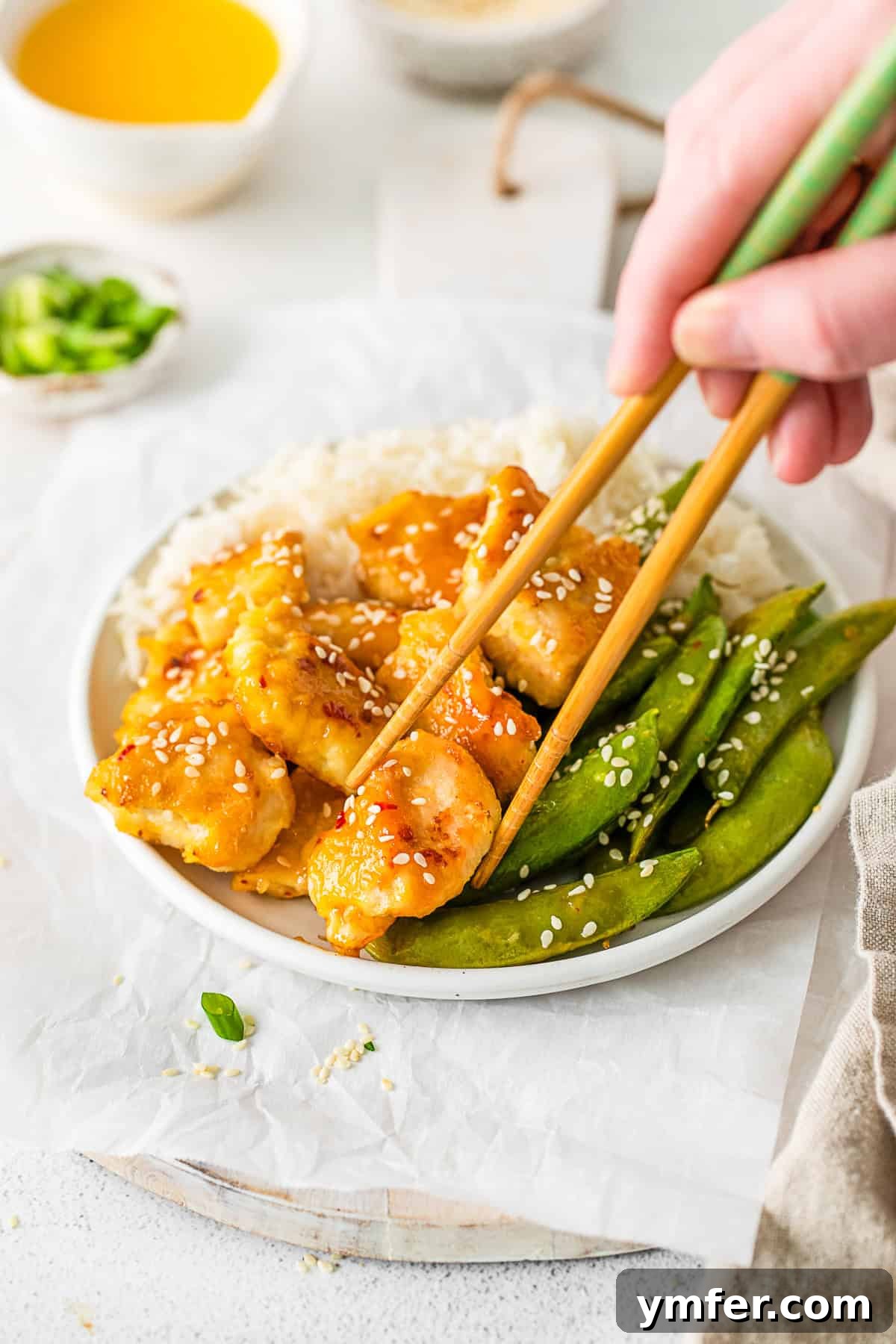 Simple Sheet Pan Sticky Orange Chicken 8 Sheet Pan Orange Chicken in a bowl with rice, garnished with sesame seeds and green onions.