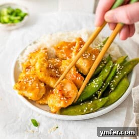 Simple Sheet Pan Sticky Orange Chicken 10 Sheet Pan Orange Chicken in a bowl with rice, garnished with sesame seeds and green onions.