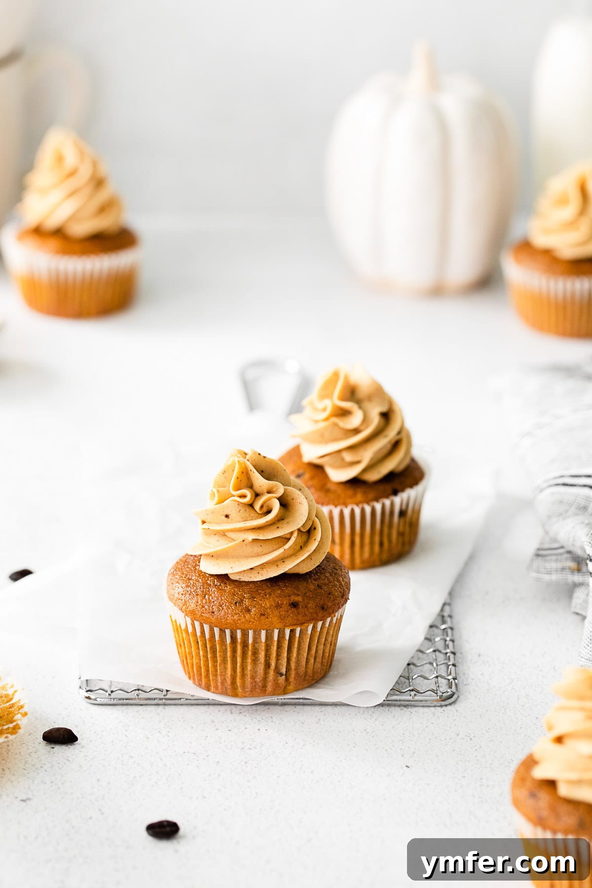 A single Pumpkin Spice Latte Cupcake in a decorative wrapper, resting on parchment paper, showcasing its perfect dome and delicate frosting swirl.