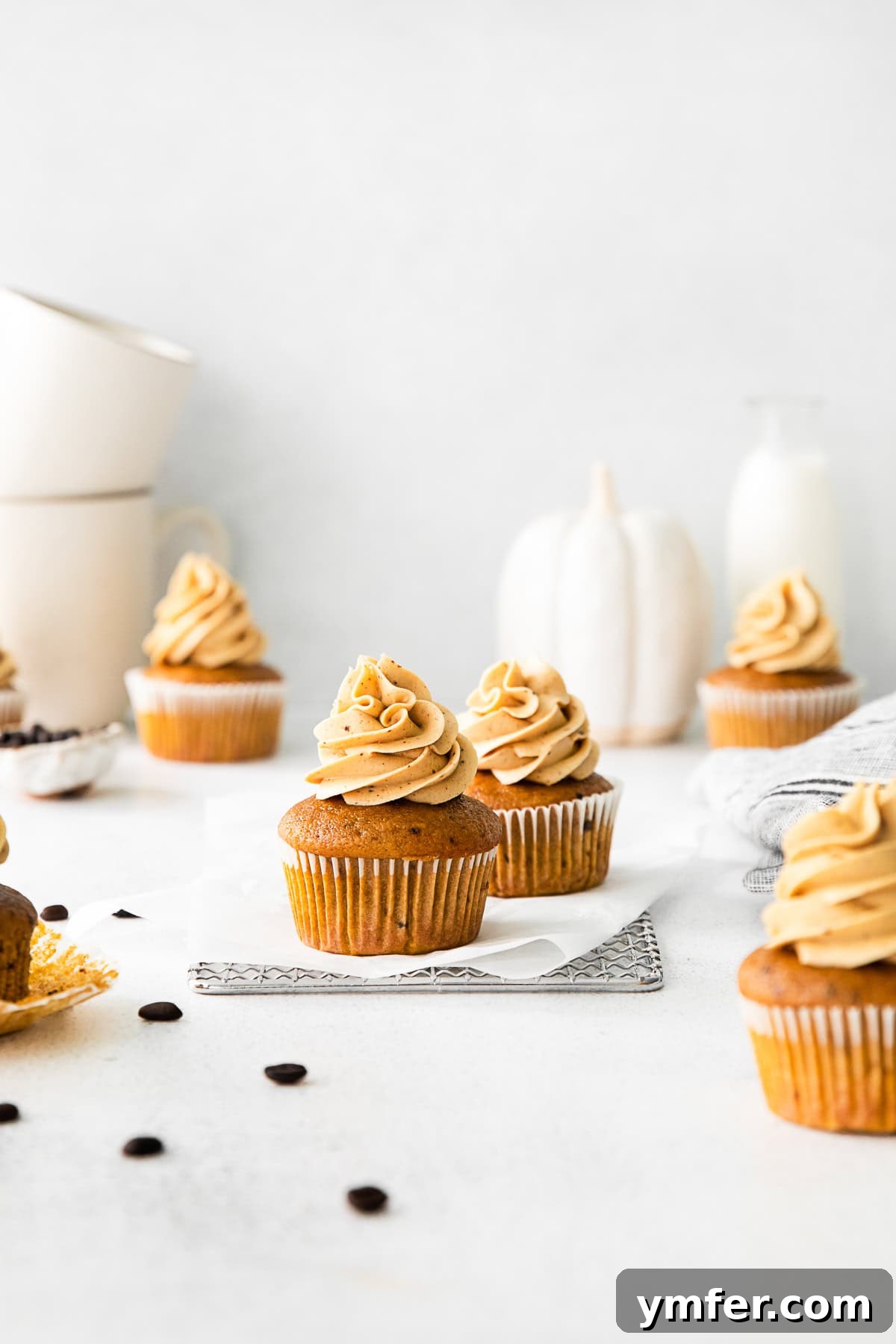 A festive display of Pumpkin Spice Latte Cupcakes on a tiered stand, surrounded by individual cupcakes, perfect for a fall gathering.