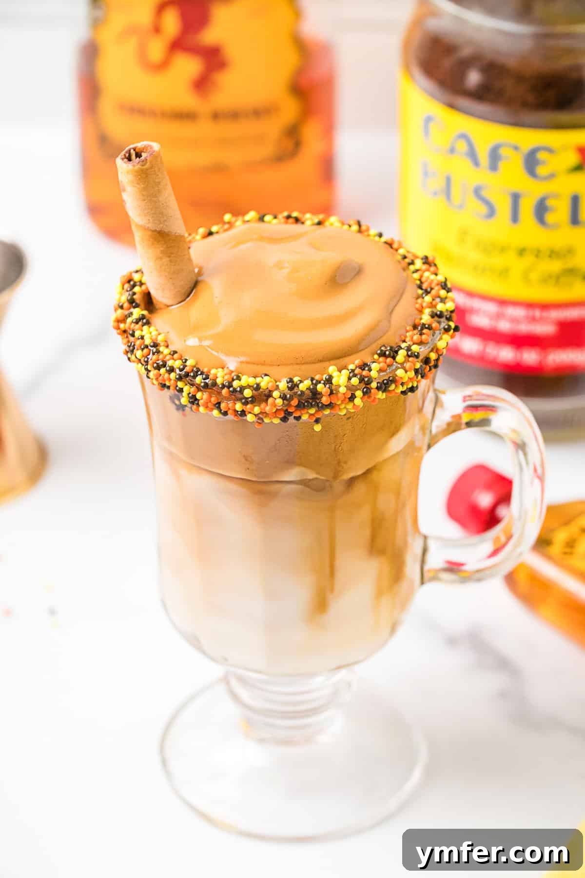 Fiery Froth Coffee 2 Fireball Whipped Coffee served in a clear glass mug, topped with a rich, fluffy coffee foam and a sprinkle of cinnamon, with a bottle of Fireball whisky in the background.