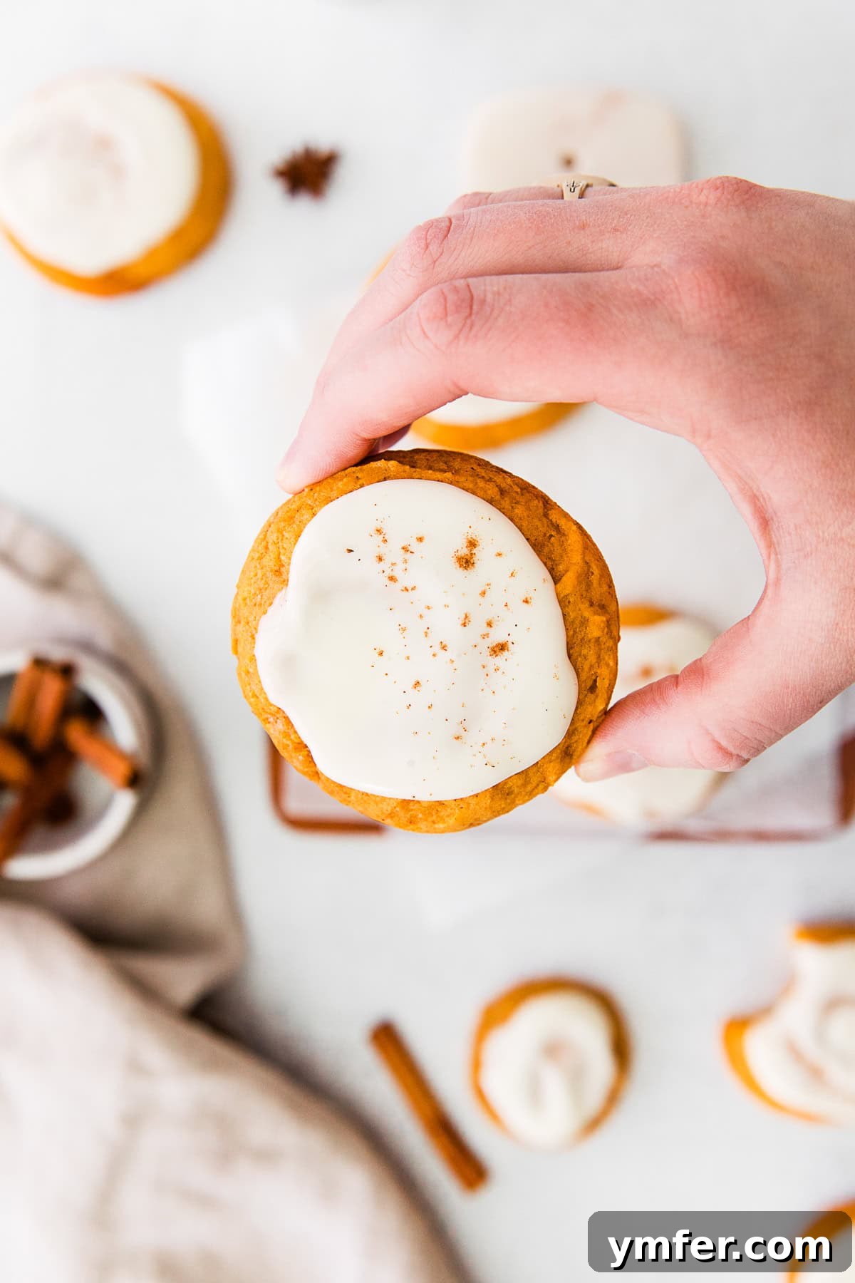 Cozy Fall Pumpkin Cookies 5 A hand holds a beautifully frosted Soft Pumpkin Cookie, showcasing its tender texture and delicious topping.