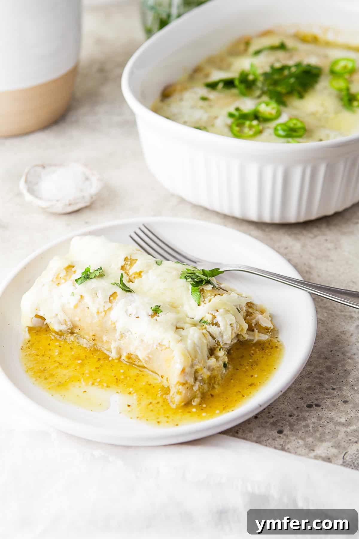 Zesty Salsa Verde Chicken Enchiladas 2 Salsa Verde Chicken Enchiladas served on a plate with a fork. A fresh sprig of cilantro garnishes the dish, highlighting its vibrant green sauce and melted cheese.