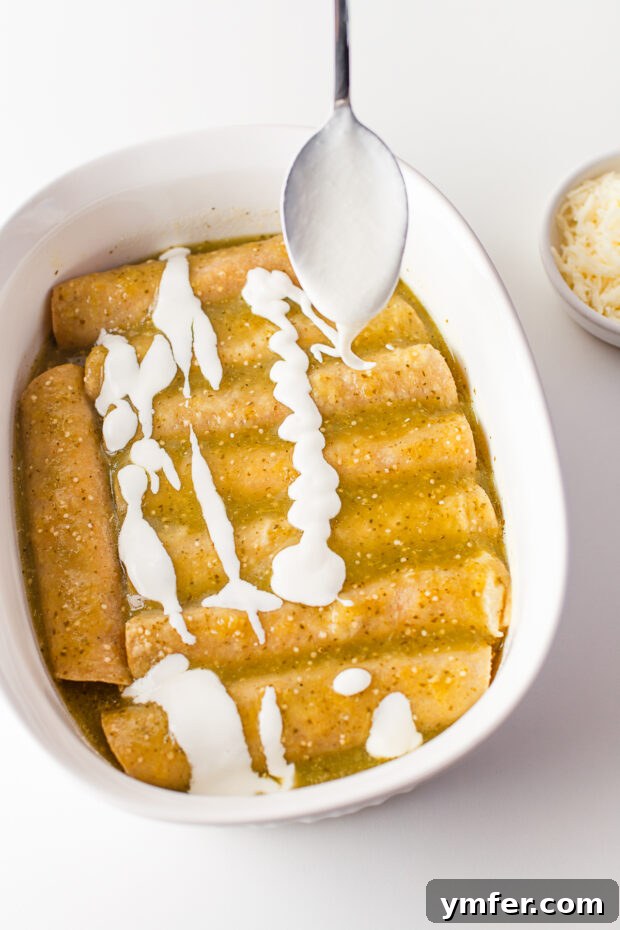 Zesty Salsa Verde Chicken Enchiladas 6 A generous drizzle of creamy sour cream cascading over a pan of freshly baked Salsa Verde Chicken Enchiladas, ready for the final layer of cheese.