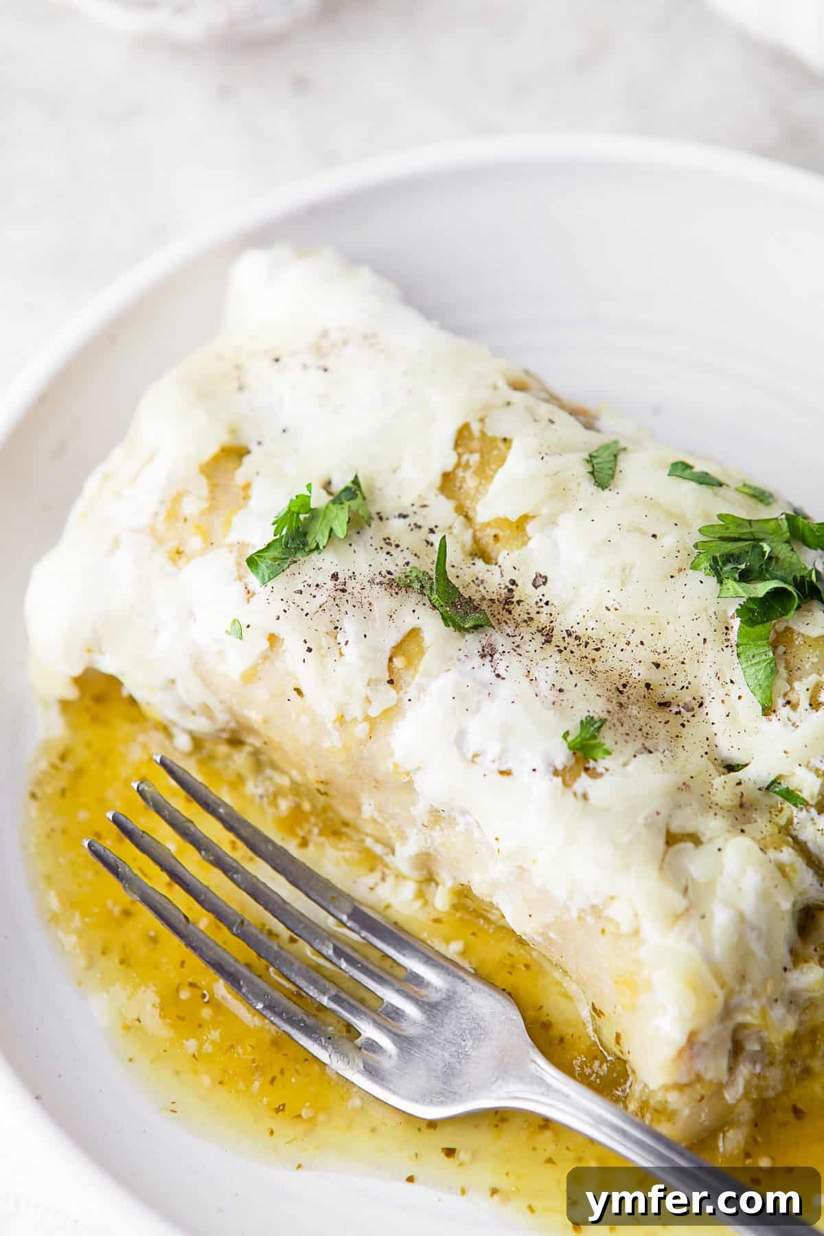 Zesty Salsa Verde Chicken Enchiladas 7 A single Salsa Verde Chicken Enchilada, generously topped with fresh cilantro, resting on a white plate with a fork, showcasing its perfectly melted cheese and vibrant green sauce.