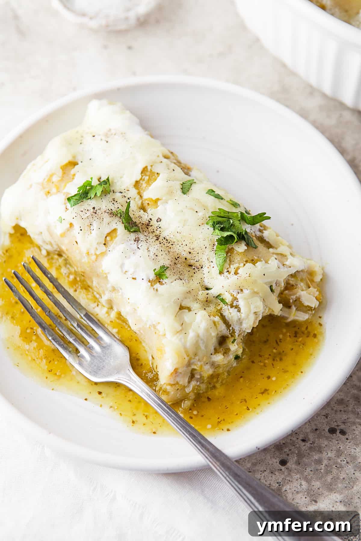 Zesty Salsa Verde Chicken Enchiladas 9 A close-up of a Salsa Verde Chicken Enchilada on a plate, perfectly cut to reveal its rich, cheesy chicken filling, ready to be enjoyed with a fork.