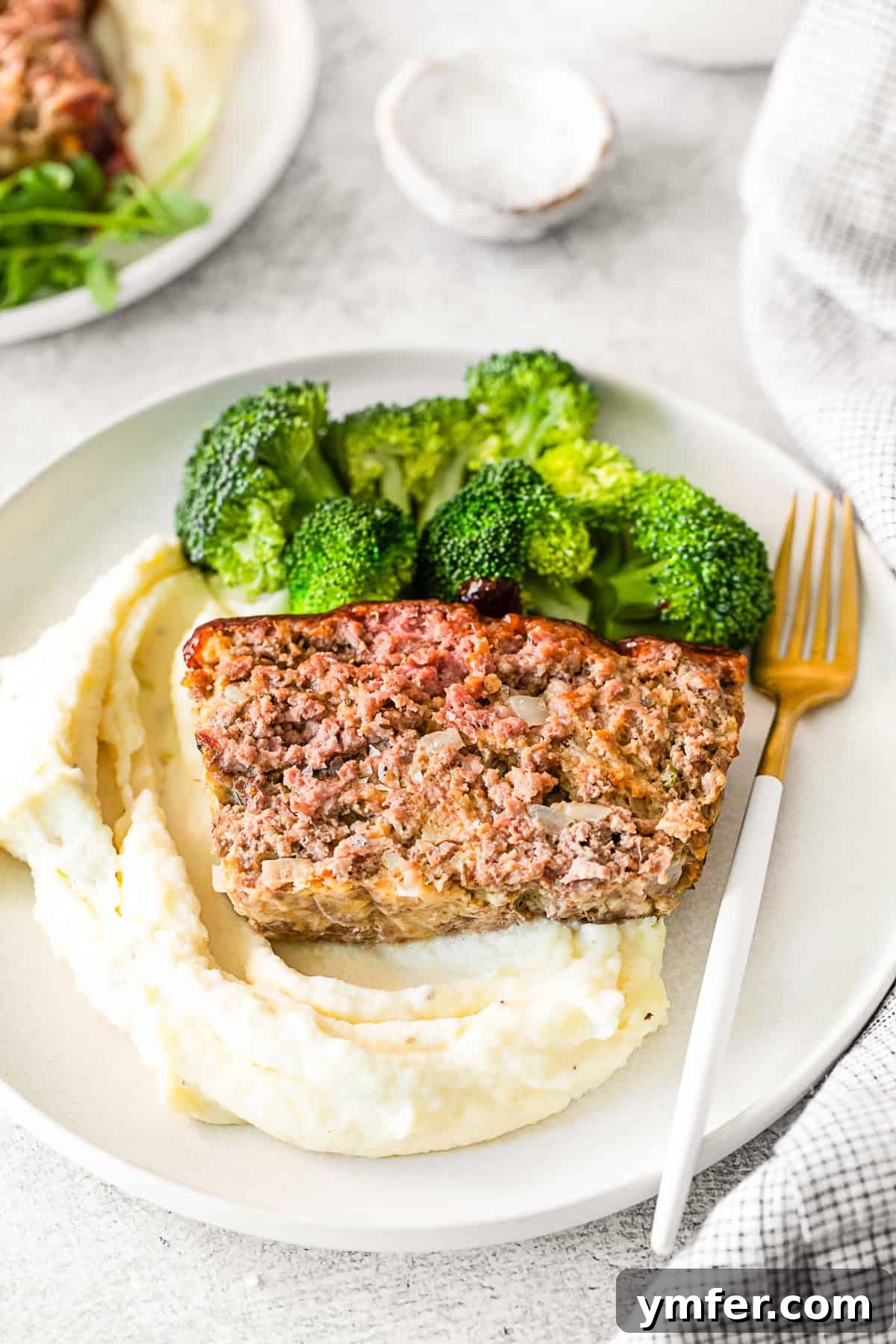 Smoky BBQ Glazed Meatloaf 8 A serving of BBQ Glazed Meatloaf, with mashed potatoes and vibrant green broccoli on a white plate.