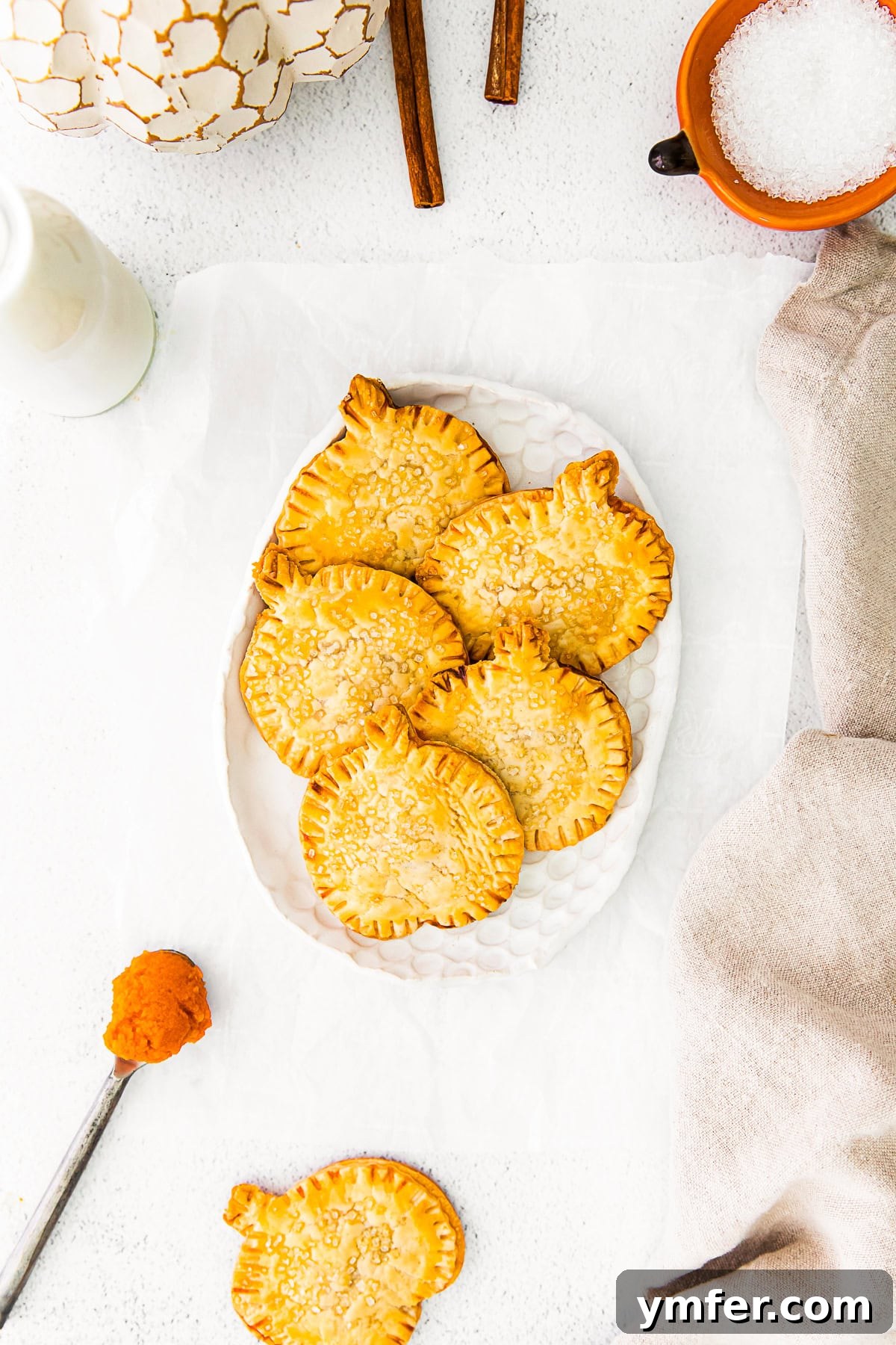 Autumn Pumpkin Pockets 2 Golden brown pumpkin hand pies arranged beautifully on a rustic white plate, garnished with a sprinkle of coarse sugar.
