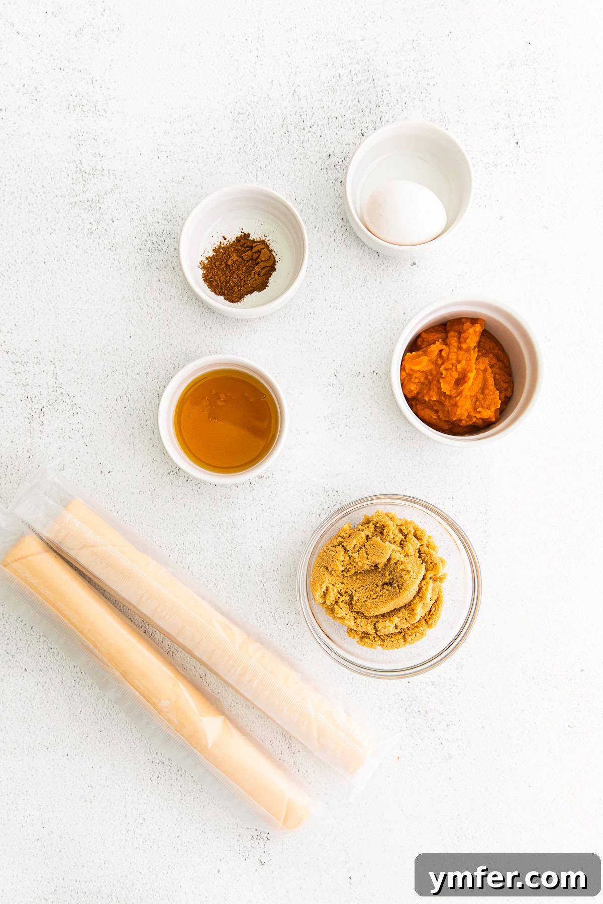 Autumn Pumpkin Pockets 3 A selection of fresh ingredients laid out on a wooden table, including a can of pumpkin puree, a bowl of brown sugar, a bottle of maple syrup, and a container of pumpkin pie spice, ready for making hand pies.