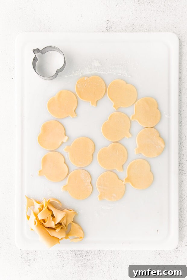 Autumn Pumpkin Pockets 5 Neatly cut pie dough shapes, some in the form of small pumpkins, arranged on a baking surface, ready for filling.