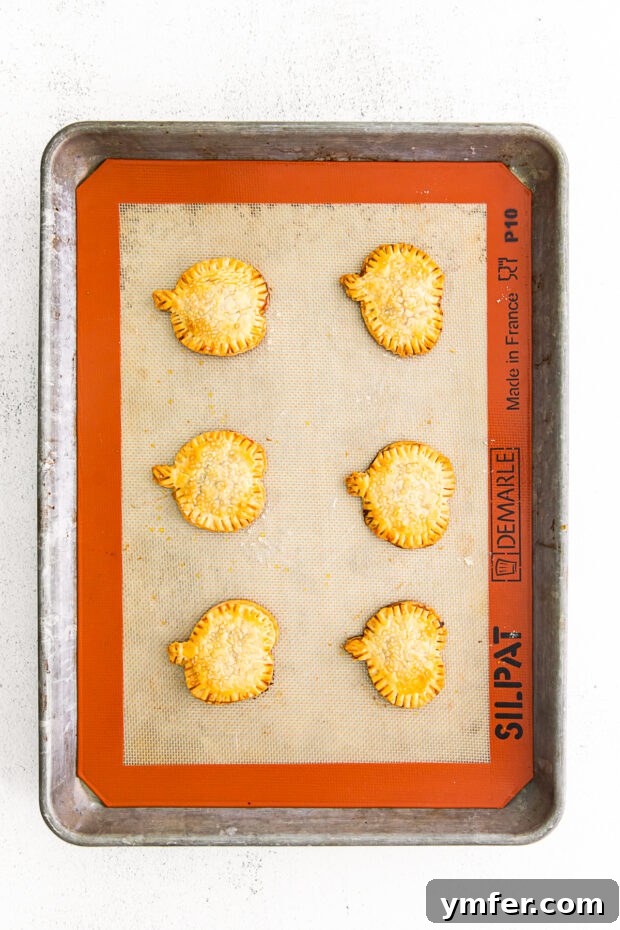 Autumn Pumpkin Pockets 7 Freshly baked and golden brown pumpkin hand pies, perfectly puffed and glistening with coarse sugar, cooling on a sheet pan.