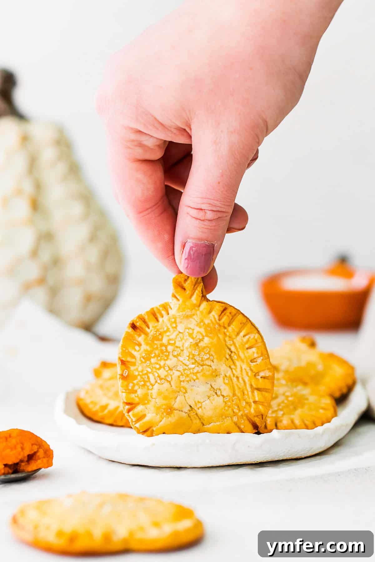 Autumn Pumpkin Pockets 8 A hand holding up a single golden pumpkin hand pie, showcasing its perfect size and crispy, sugar-dusted crust.