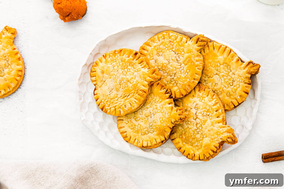 Autumn Pumpkin Pockets 10 A stack of perfectly baked pumpkin hand pies, golden brown and sprinkled with coarse sugar, displayed on a beautiful white serving platter.